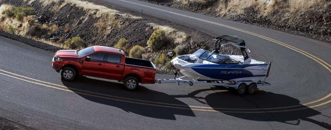 A red 2023 Ford Ranger XLT is shown towing a boat around a corner.
