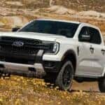 A white 2024 Ford Ranger FX4 is shown driving through a field.