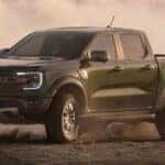 A dark green 2024 Ford Ranger Raptor is shown kicking up dust.