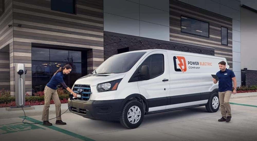 A white 2023 Ford E-Transit van is shown parked and charging.
