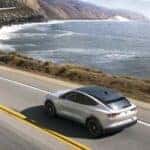 A black and white 2023 Ford Mustang Mach-E is shown driving near an ocean after viewing electric cars for sale.