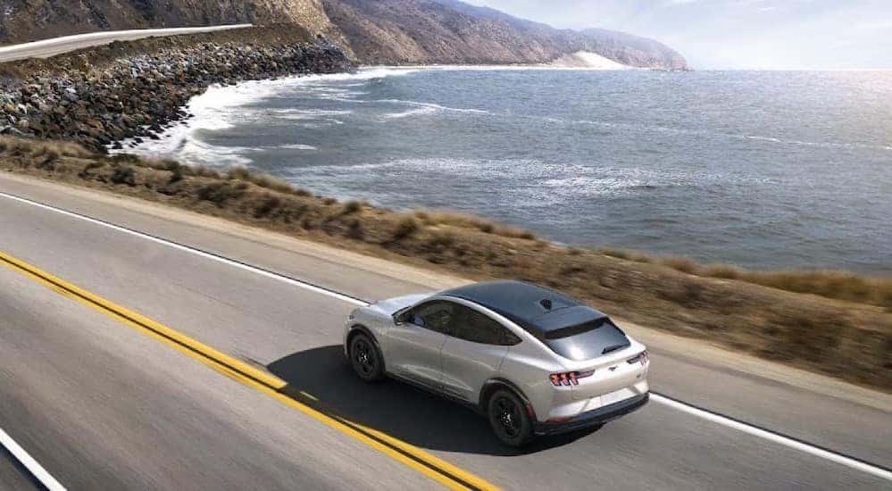 A black and white 2023 Ford Mustang Mach-E is shown driving near an ocean after viewing electric cars for sale.