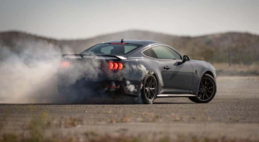 A black 2024 Ford Mustang Dark Horse is shown doing a burnout on a track.