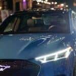 A blue 2024 Ford Mustang Mach-E for sale is shown parked on a city street.