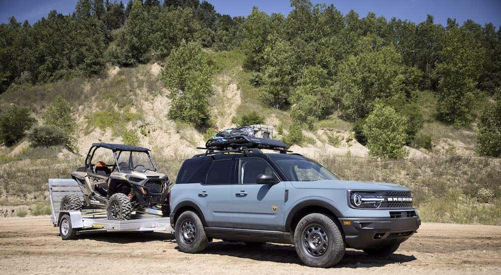A blue 2024 Ford Bronco Sport Badlands is shown from the front at an angle while towing a UTV.
