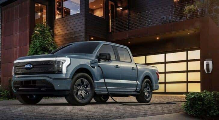 A silver 2023 Ford F-150 Lightning plugged into a home charging station.