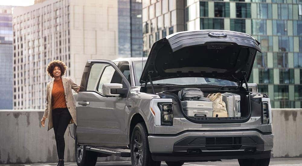 A woman loading luggage into the open frunk of her silver 2024 Ford F-150 Lightning.