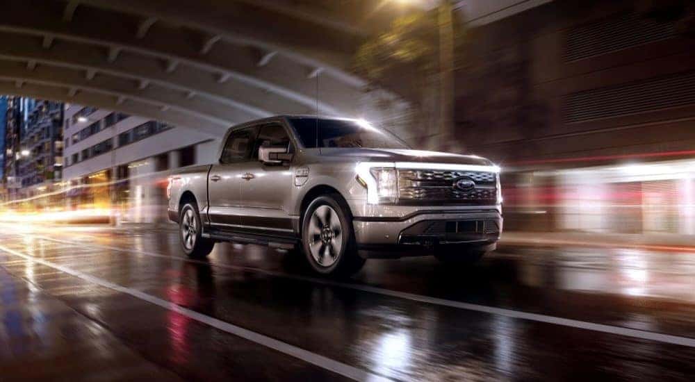 A silver 2024 Ford F-150 Lightning driving on a wet city road at night.