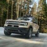 A tan 2024 Ford Bronco Sport Badlands driving on a wooded road.
