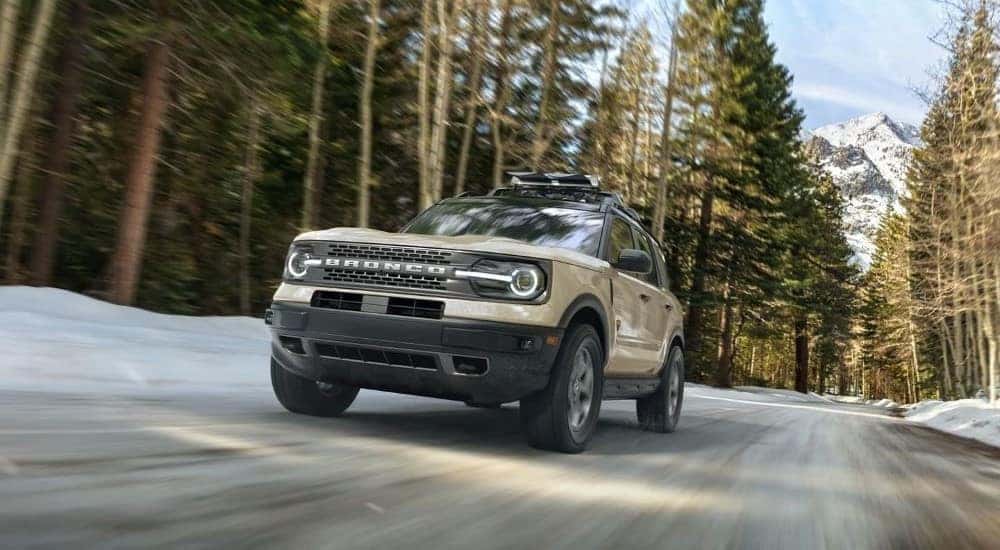 A tan 2024 Ford Bronco Sport Badlands driving on a wooded road.