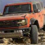 A red 2024 Ford Bronco Raptor off-roading over dusty rocks.