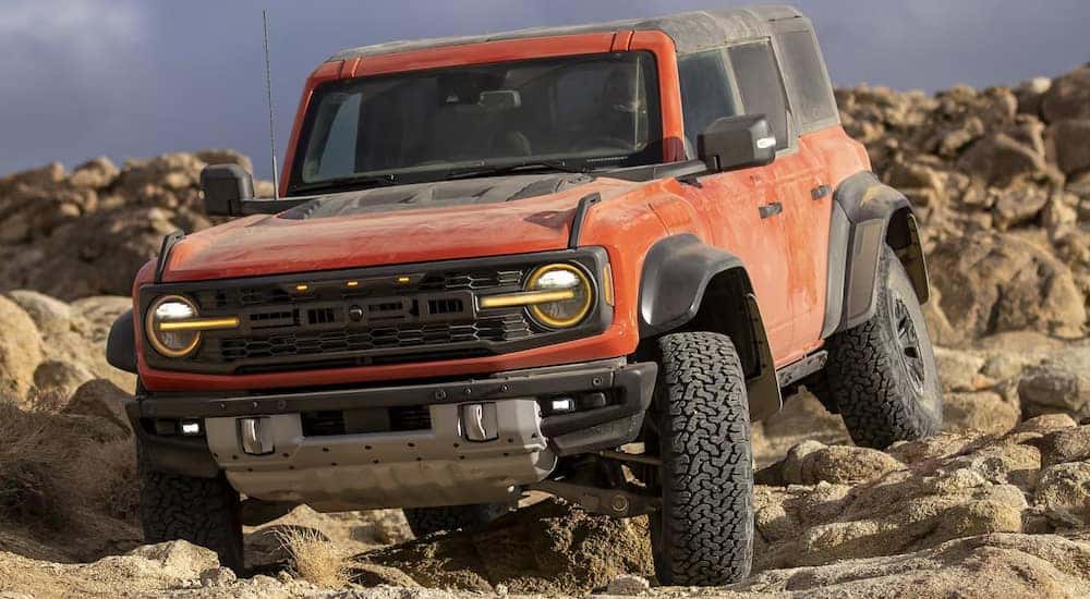 A red 2024 Ford Bronco Raptor off-roading over dusty rocks.