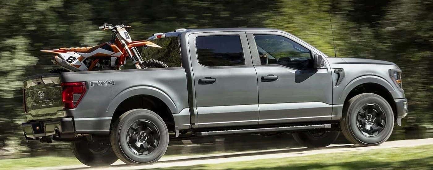 A gray 2024 Ford F-150 is shown driving on a dirt road after viewing a Ford F-150 for sale in Cincinnati.