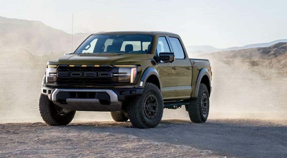 A green 2024 Ford F-150 Raptor is shown parked off-road.