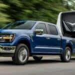 A blue 2024 Ford F-150 Tremor is shown towing a trailer.