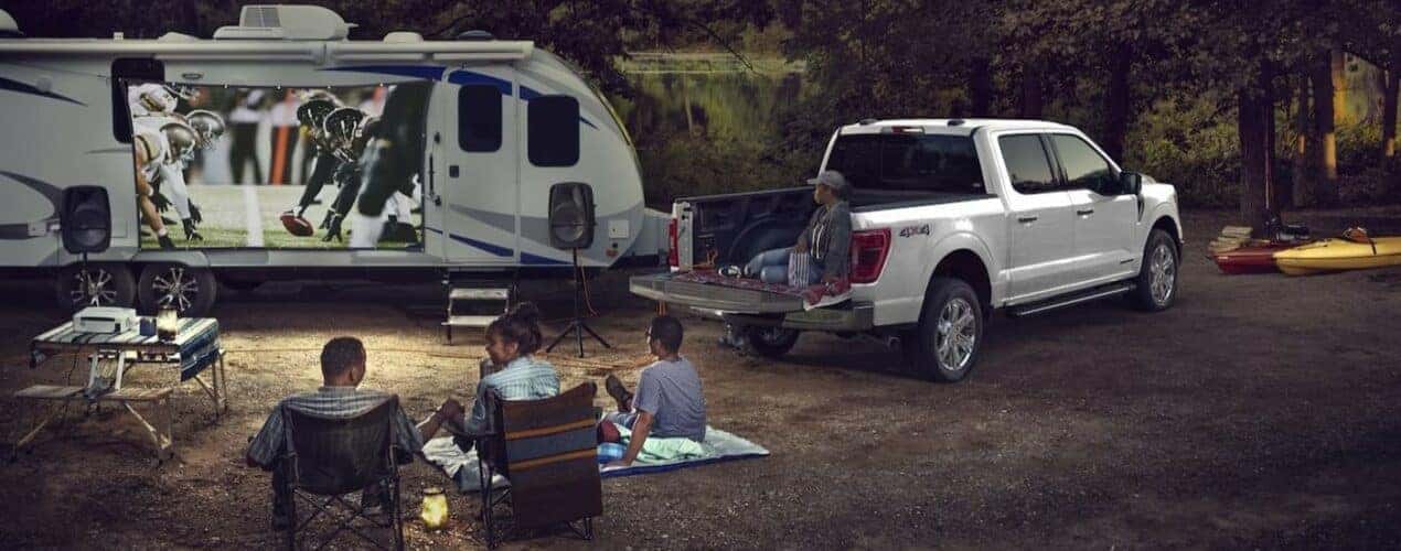 A white 2024 Ford F-150 is shown parked near a trailer on a campsite.