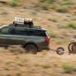 A green 2025 Ford Expedition Tremor is shown towing a trailer off-road.