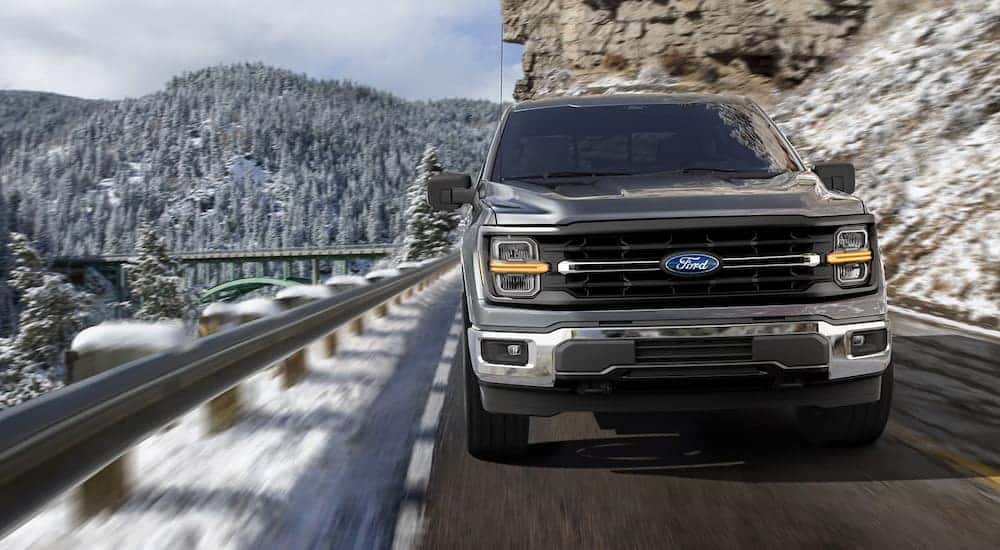 Front view of a grey 2025 Ford F-150 driving on a mountain road.