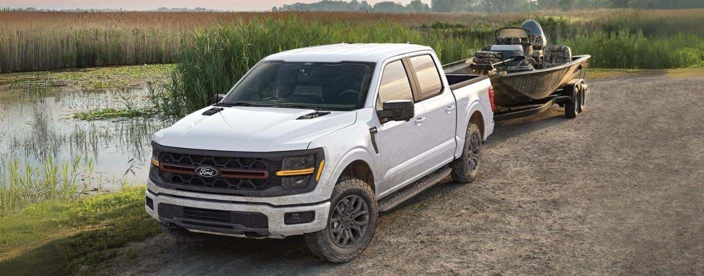 A white 2025 Ford F-150 Tremor is shown towing a boat after visiting a Ford dealer near Bellevue.