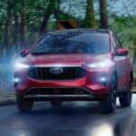 A red 2025 Ford Escape driving on a wet road with its headlights on.