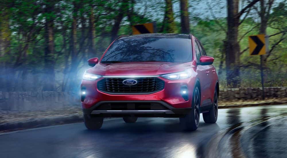 A red 2025 Ford Escape driving on a wet road with its headlights on.