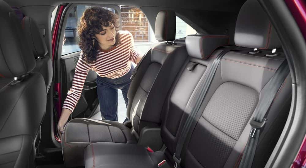 A woman leaning in to adjust the back seats in a red 2025 Ford Escape.