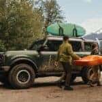 A couple unloading a kayak from the roof of a green 2025 Ford Bronco Badlands.