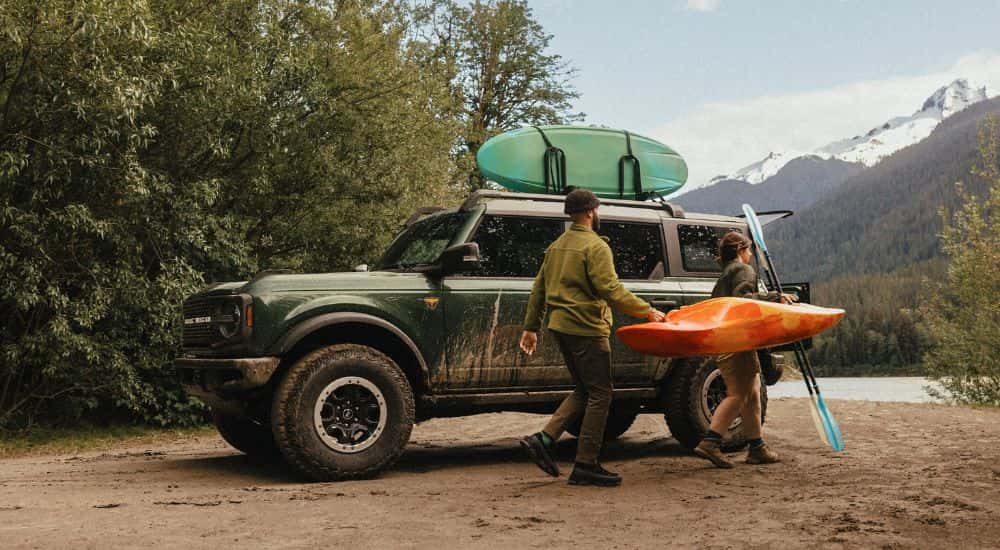 A couple unloading a kayak from the roof of a green 2025 Ford Bronco Badlands.