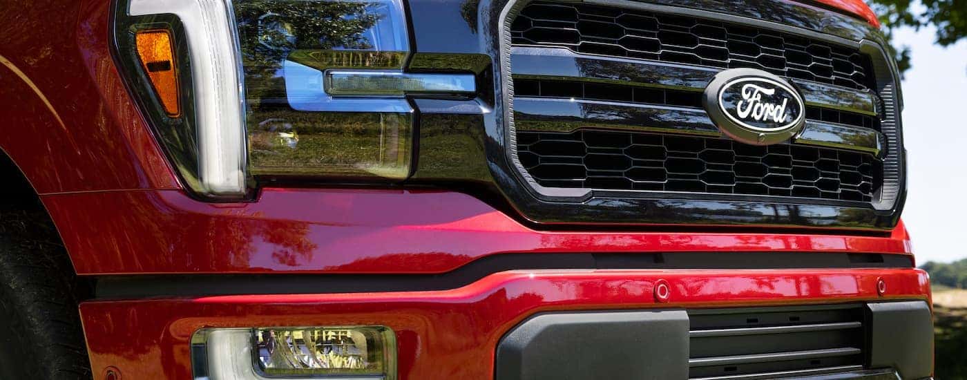 A close up of the grille and headlight on a red 2024 Ford F-150 Lariat.