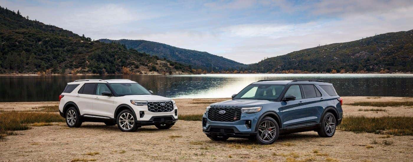 A white and a blue 2025 Ford Explorer are shown from the front.