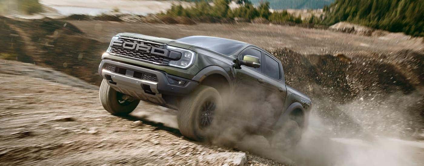 Green 2025 Ford Ranger Raptor off-roading on a dusty road.
