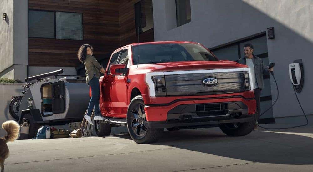 A red 2025 Ford F-150 Lightning charging while a couple packs a camper