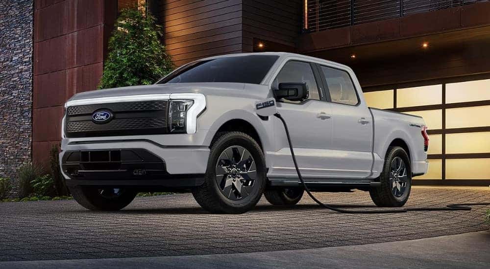 A gray 2025 Ford F-150 Lightning charging in a driveway