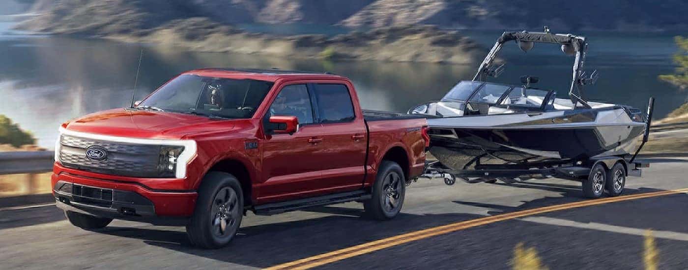 A red 2025 Ford F-150 Lightning towing a boat near a lake.