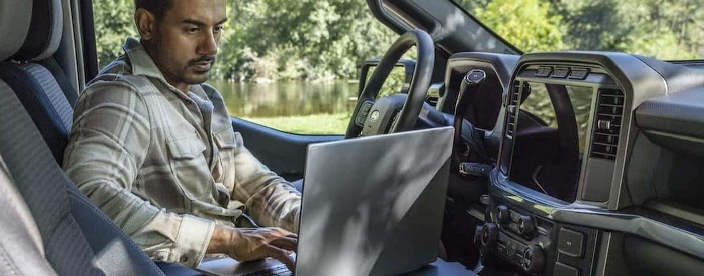 A person using a laptop in a 2025 Forf F-150 for sale near Hyde Park.