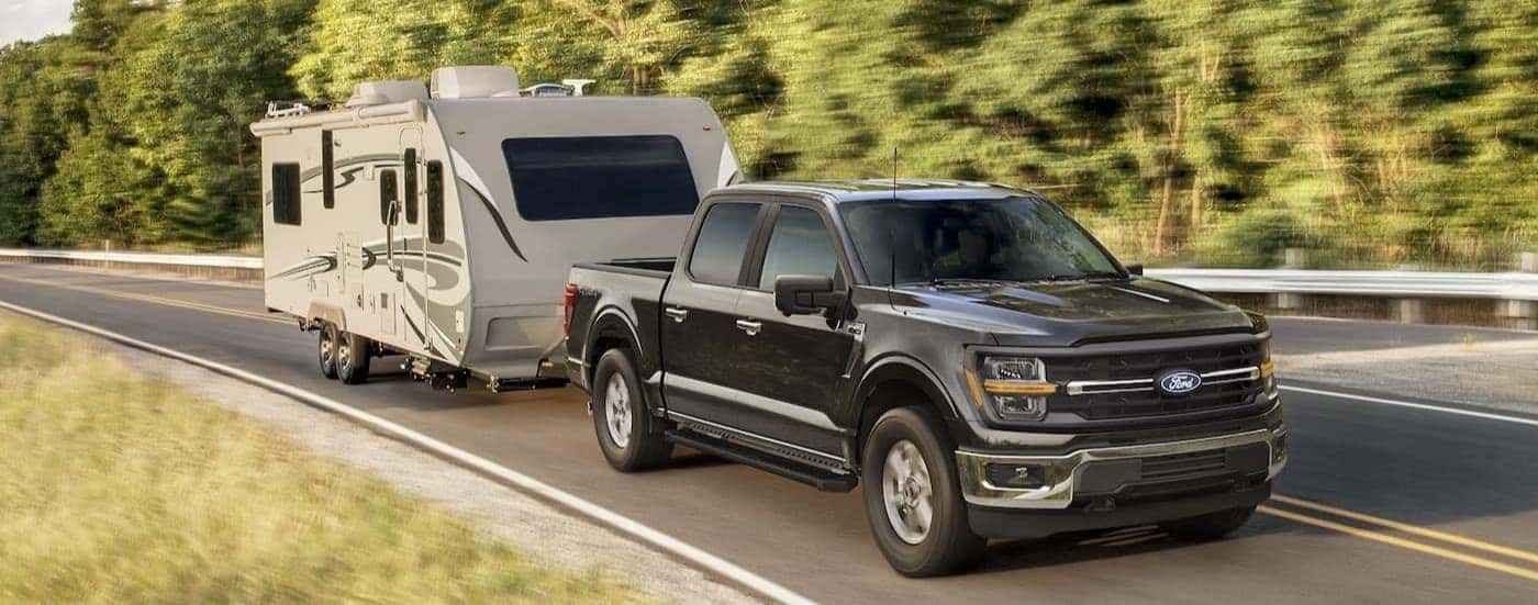 A black 2025 Ford F-150 towing a camper.