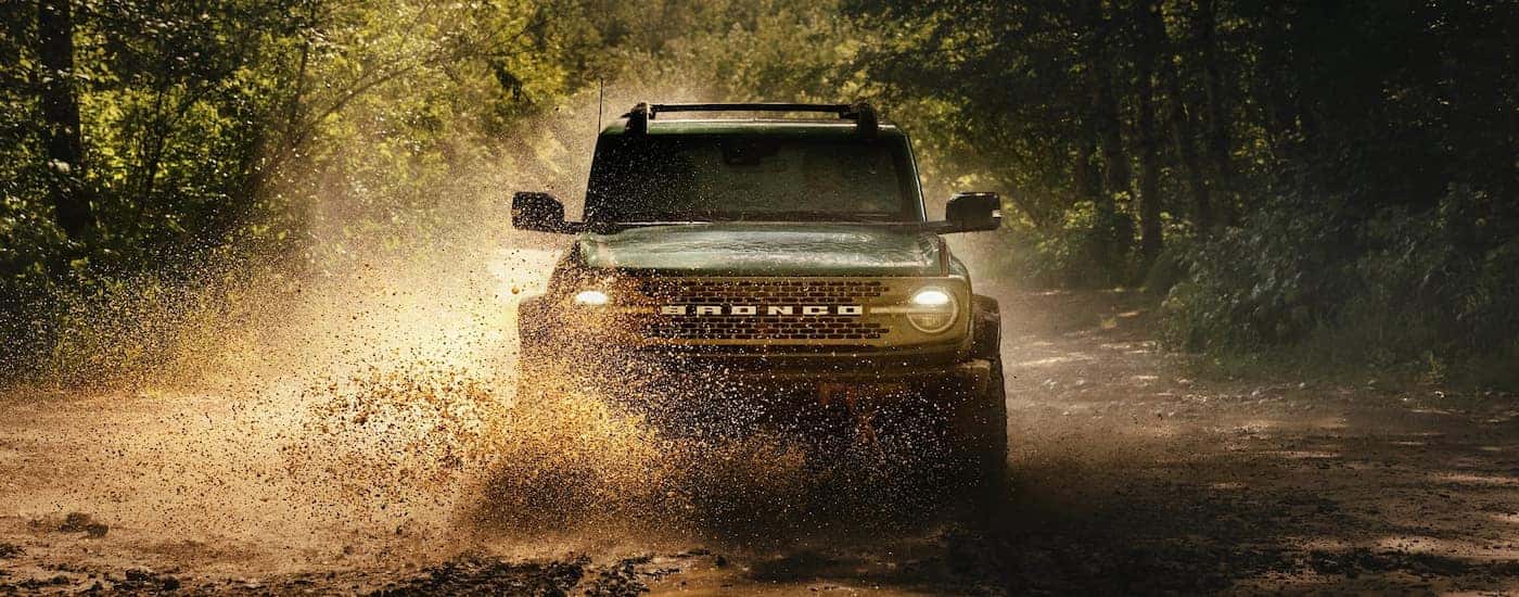 Green 2025 Ford Bronco for sale near Northgate driving over a muddy trail.