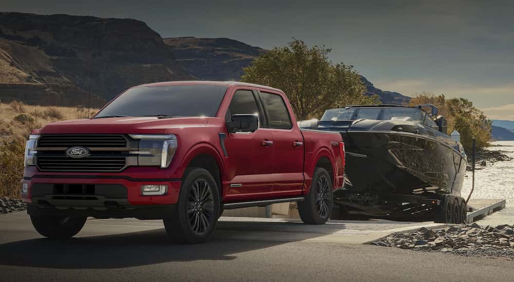 Red 2025 Ford F-150 STX towing a boat out of a lake.