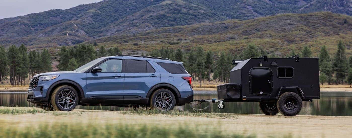 A blue 2025 Ford Explorer ST-Line towing a trailer off-road.