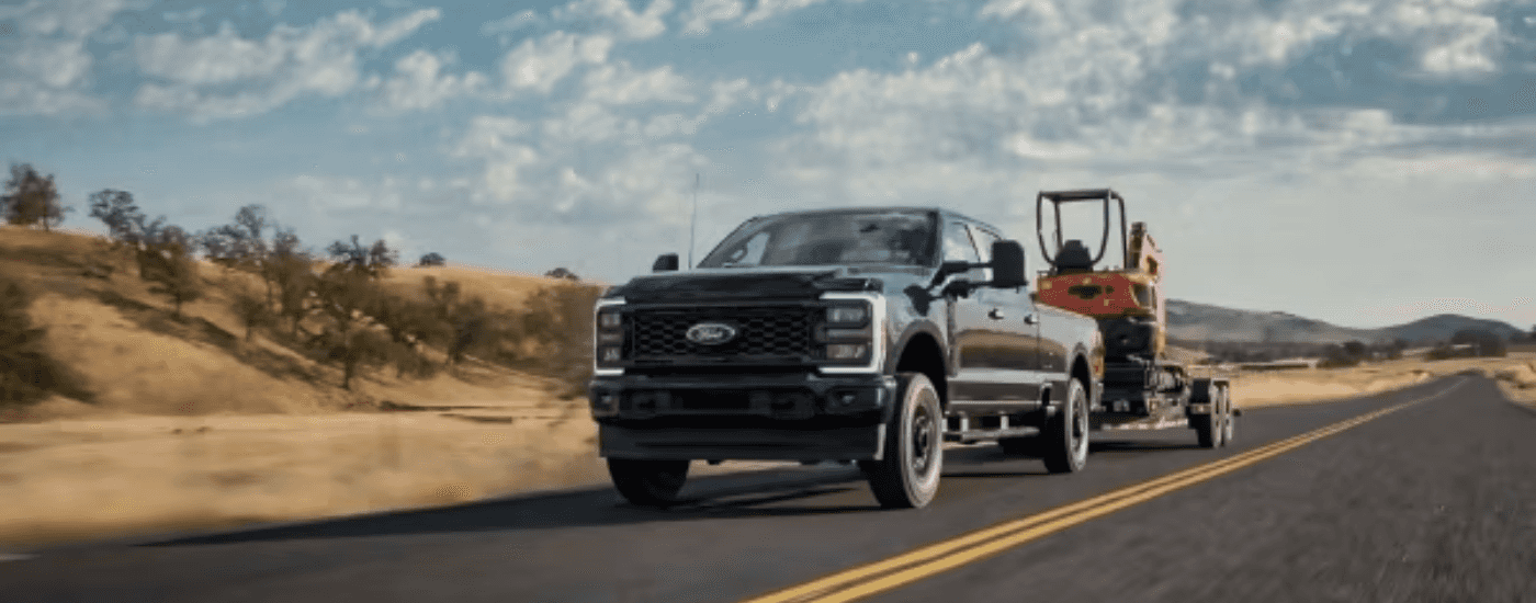 Grey 2026 Ford F-250 Super Duty towing a backhoe