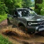 Silver 2026 Ford Bronco driving off-road through a forest.