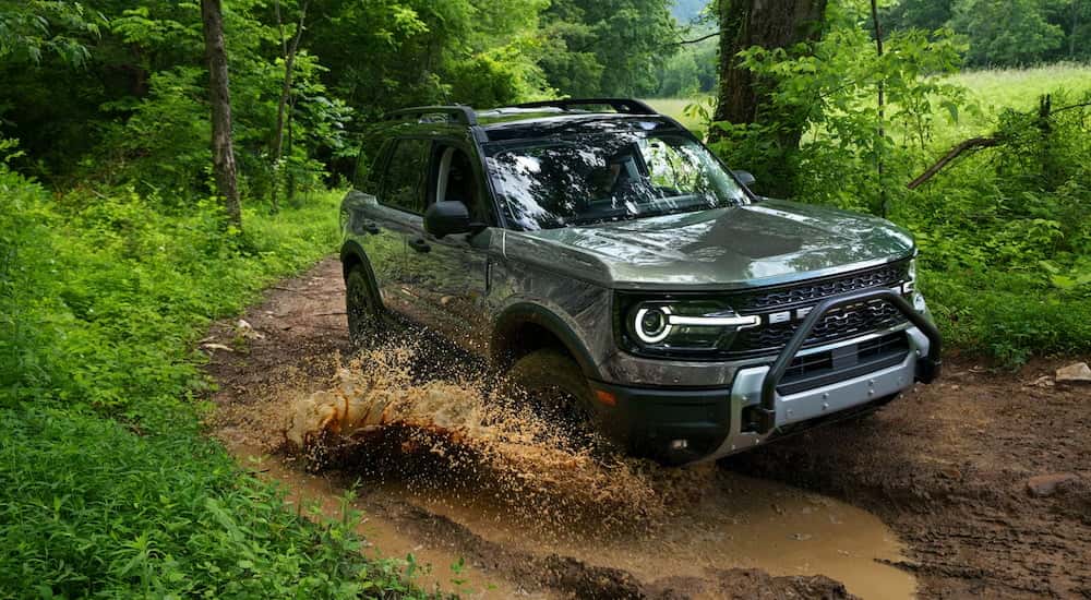 Silver 2026 Ford Bronco driving off-road through a forest.