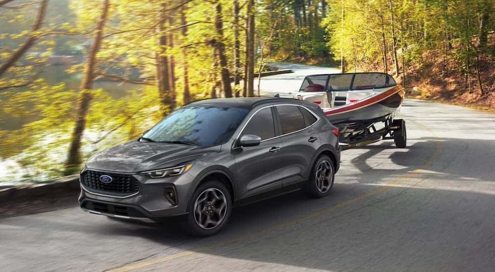 Grey 2026 Ford Escape towing a boat down a road.