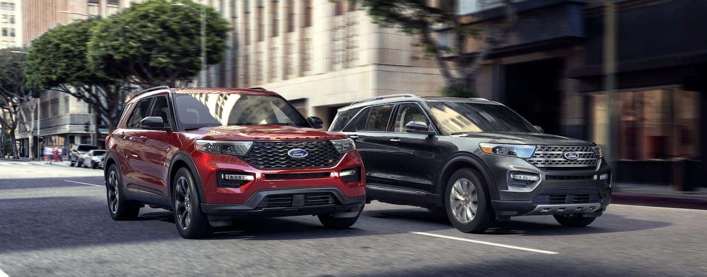 A red and a grey 2021 Ford Explorer are driving on a city street.