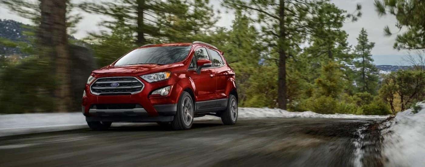 A red 2021 Ford EcoSport driving a snow-lined road.
