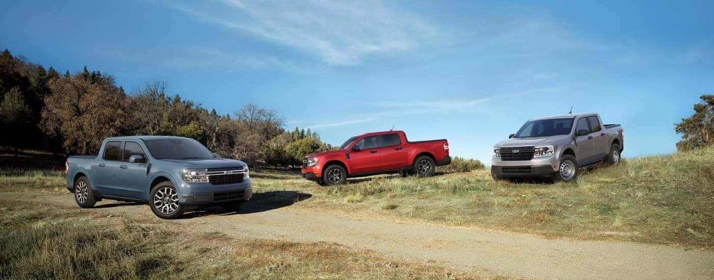 A blue, a red, and a silver 2022 Ford Maverick are shown near a dirt path and trees.
