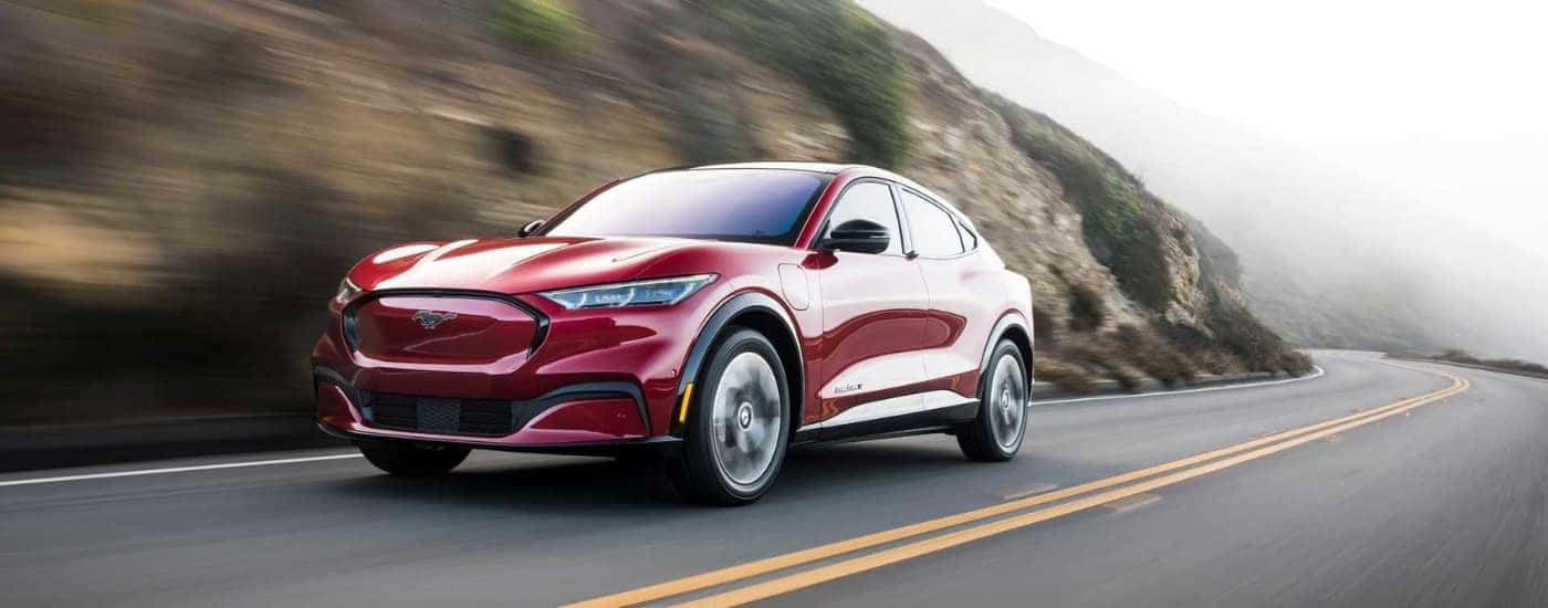 A red 2023 Ford Mustang Mach-E is shown driving past a rock.