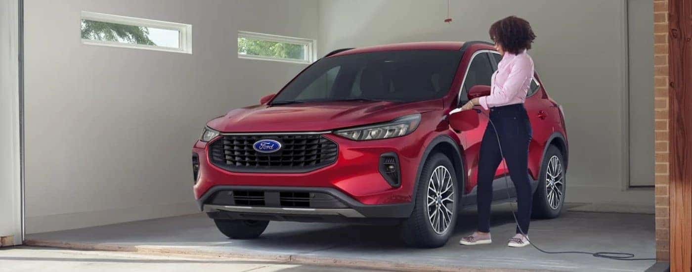 A red 2023 Ford Escape Hybrid getting plugged into a garage charger.