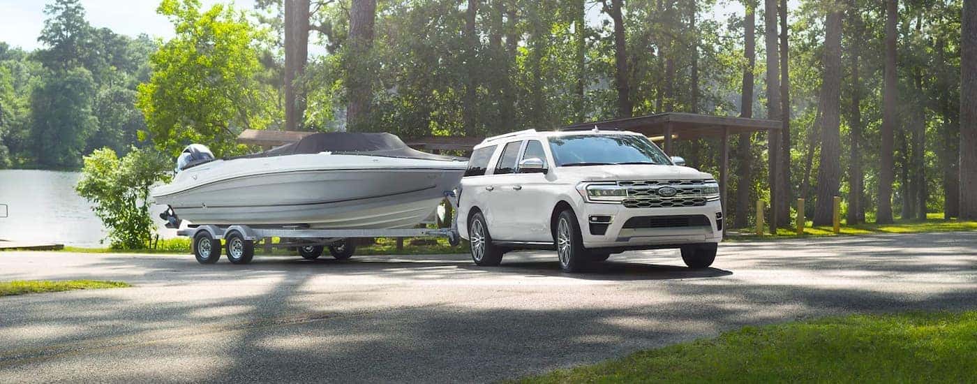 A white 2023 Ford Expedition towing a boat near a lake.