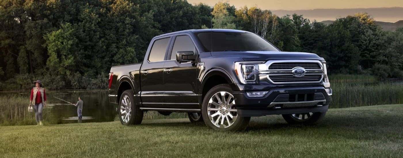 A black 2021 Ford F-150 is parked on grass in front of a couple fishing.